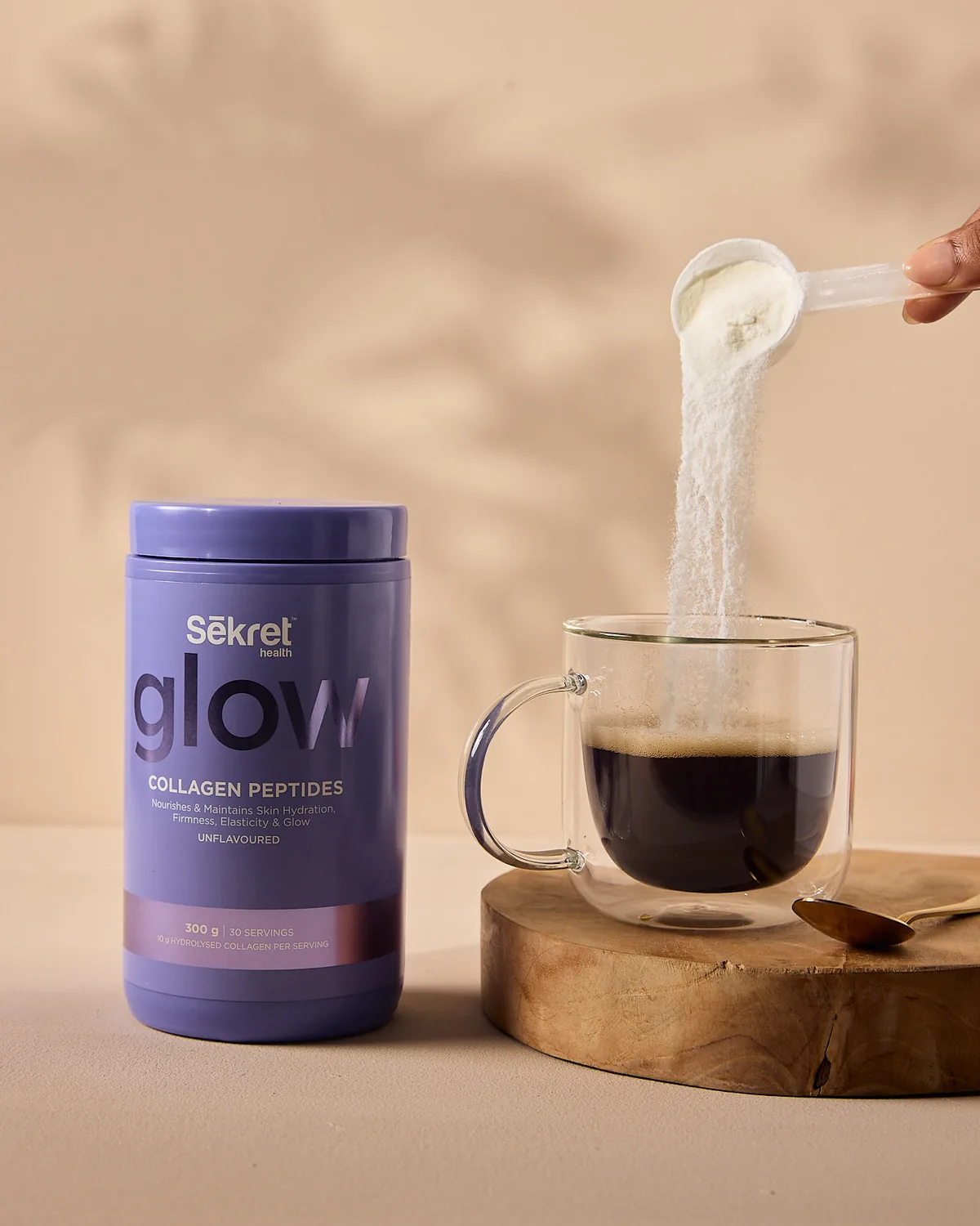 A scoop of Sēkret Glow collagen peptides poured into a glass of coffee beside the tub