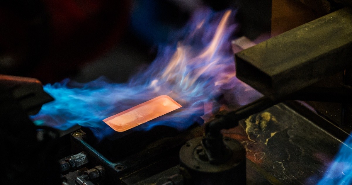 A young person with curly hair smiles at the camera while sitting in front of a laptop against a dark background.