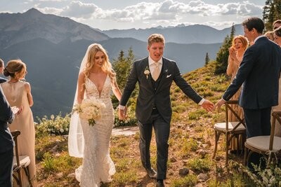 The newlyweds walk hand in hand away from the ceremony as guests watch.
