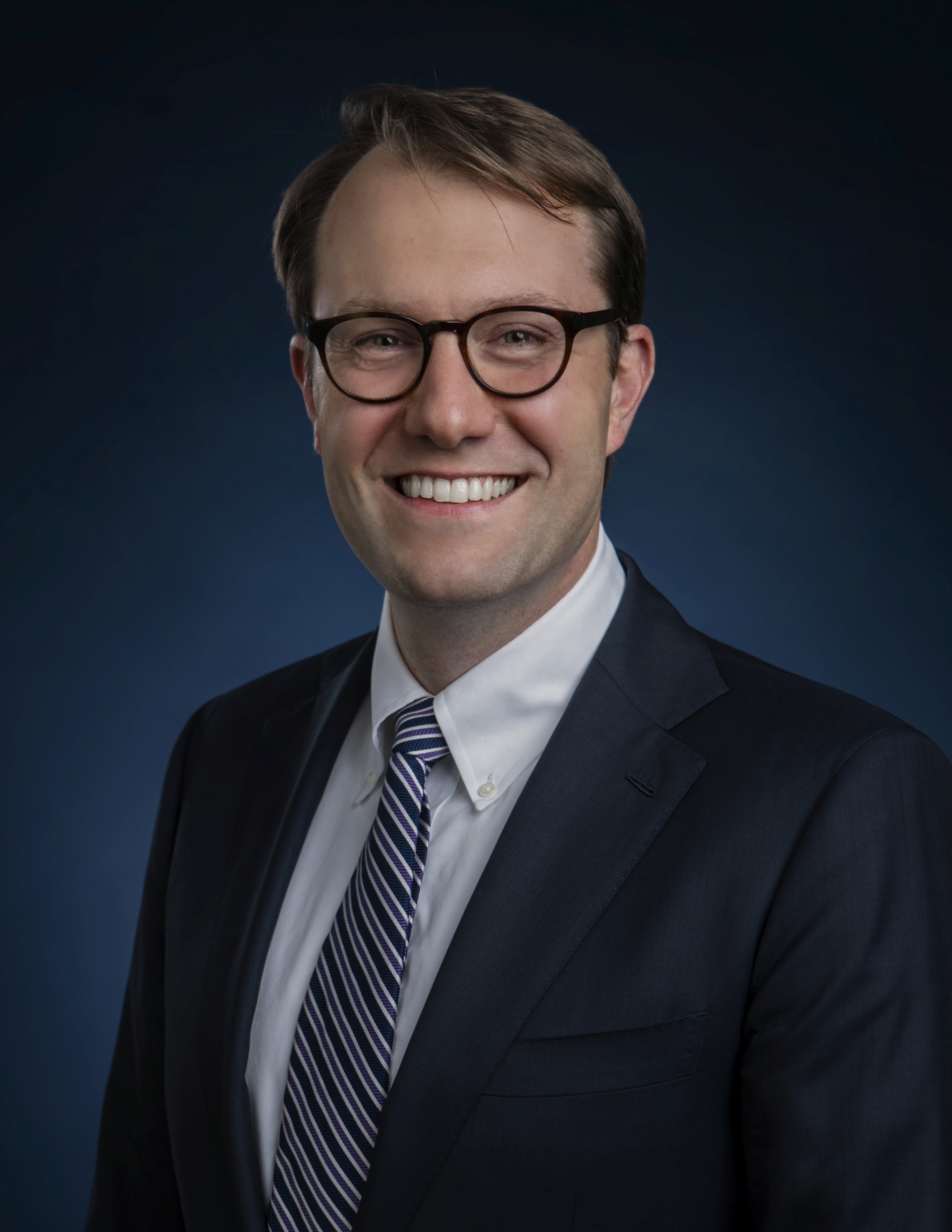 Headshot of a man wearing glasses and suit and tie.