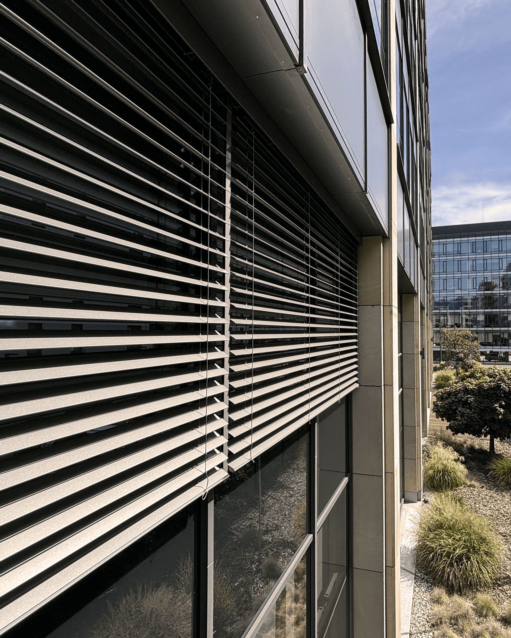 Duże szare żaluzje fasadowe zamontowane na biurowcu. Profesjonalna realizacja wykonana w Warszawie.