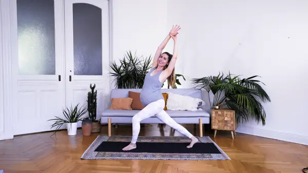 Pregnant woman in a standing hip-opening yoga stretch with arm raised – Day 8 prenatal yoga for low back pain relief and pelvic space through supportive stretches