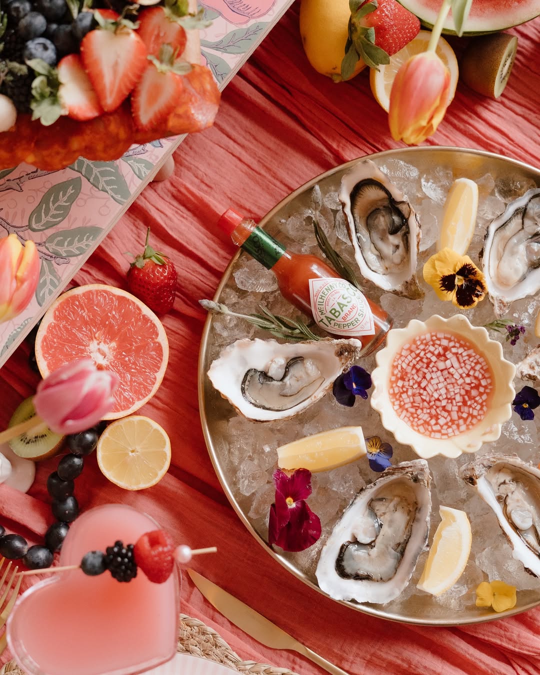 Fresh oysters on ice with strawberries, grapefruit, and a pink heart-shaped drink.