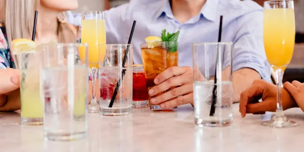 Close-up of people at a table with various colorful drinks, including iced tea, lemonade, and cocktails, garnished with lemon and mint.