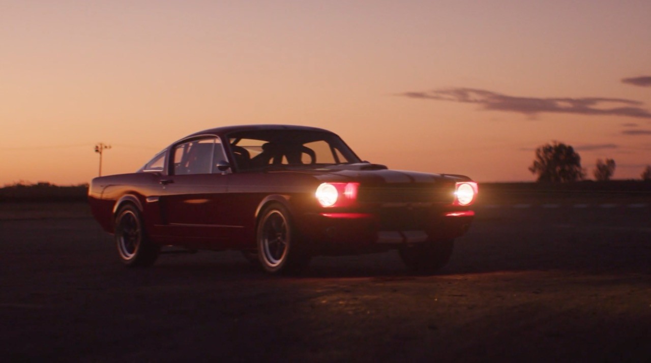 Classic muscle car parked on an open road at dusk, headlights glowing.