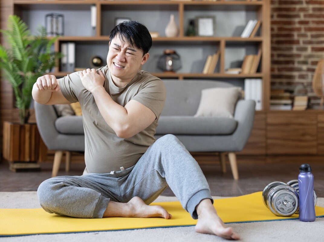 man wincing in pain after injuring himself during an intense workout routine to lose weight at home