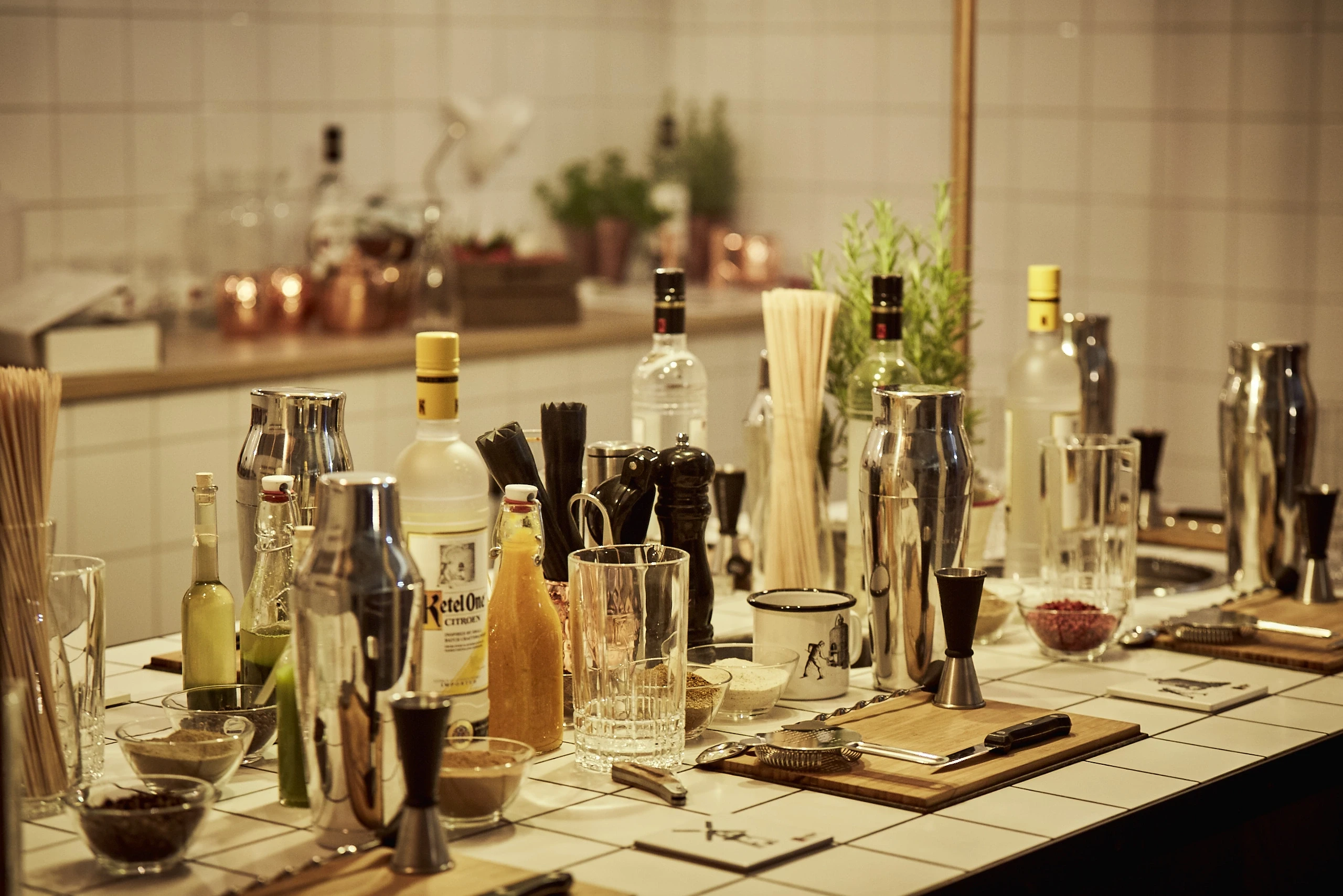 Cocktail workshop table at DIAGEO BCB17 with shakers, jiggers, Ketel One bottles and bar tools laid out on white tiles.