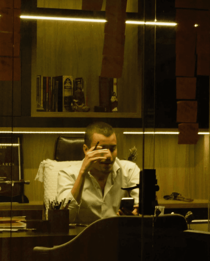 A confident person with short, styled hair and a leather jacket poses against a dark backdrop.