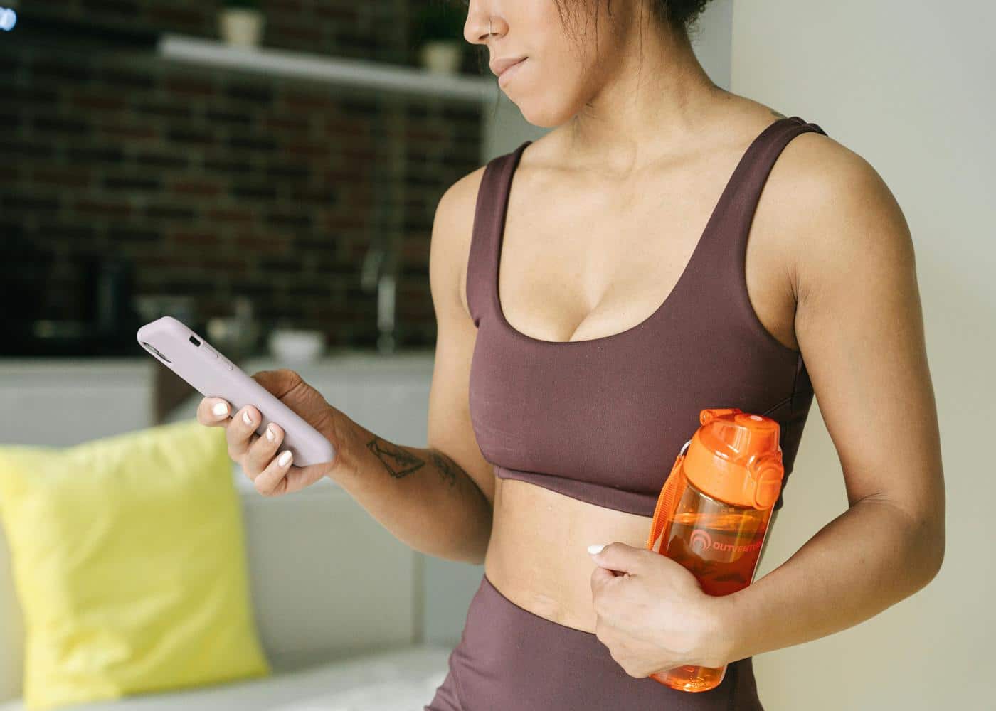 Woman in workout clothes holding water bottle on one hand and smartphone on the other