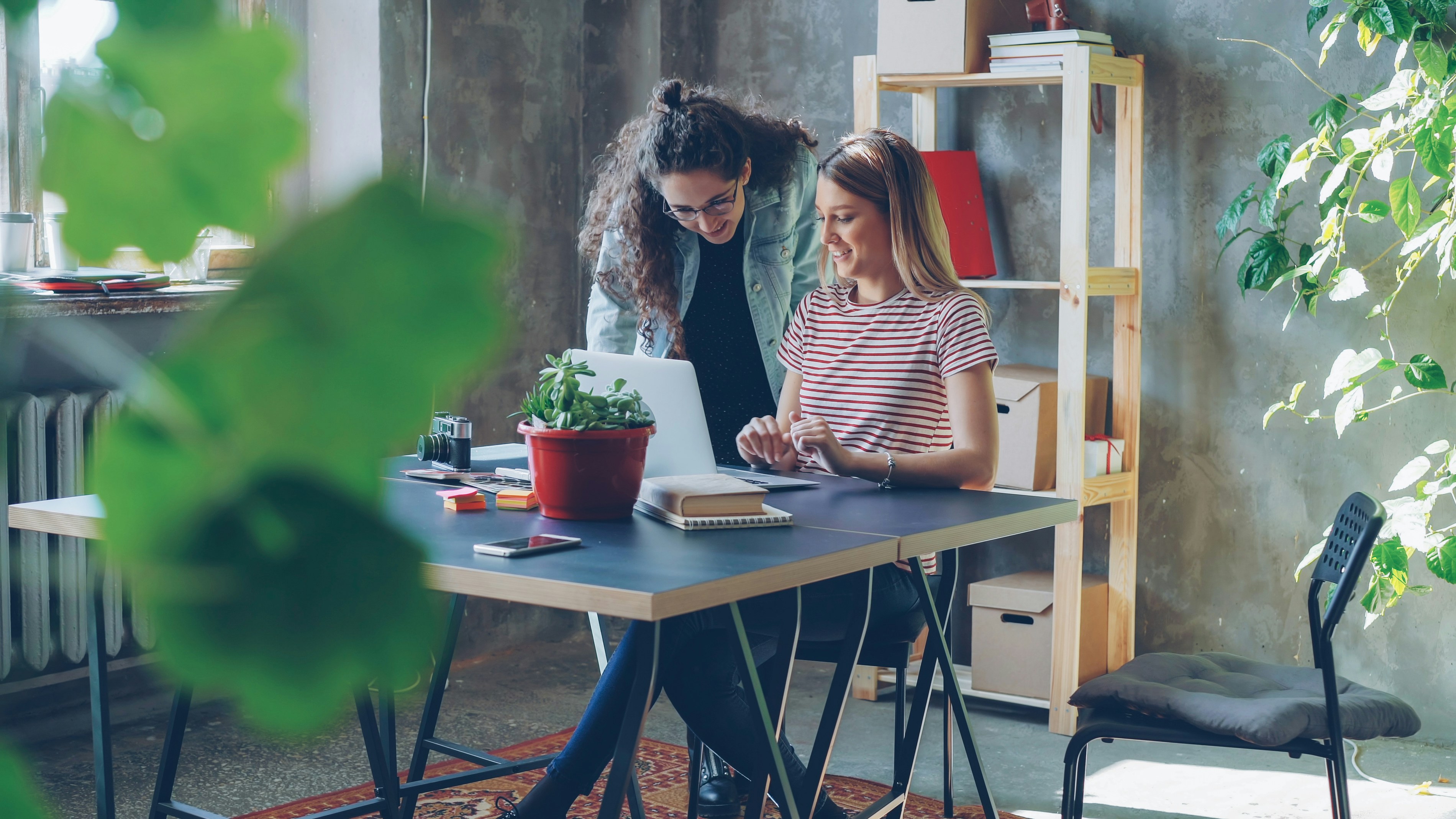 Two women collaborate at a laptop in an office.