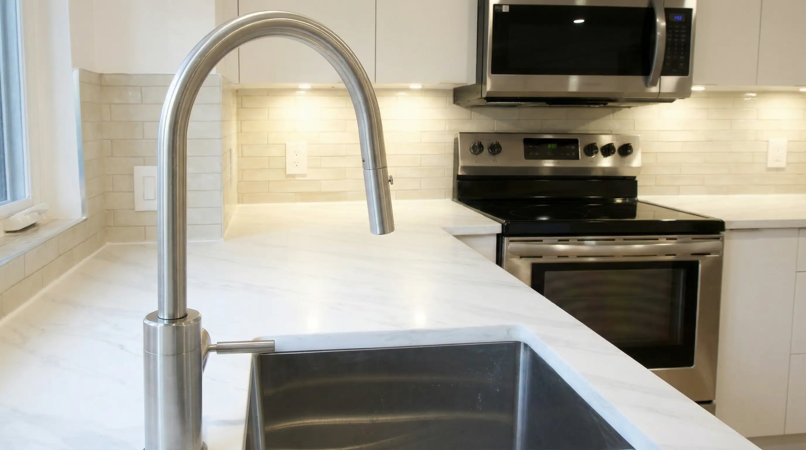 Kitchen detail in Vancouver Custom Homes' West 16th Vancouver multiplex showcasing a quartz countertop, stainless gooseneck faucet, under-cabinet lighting, and subway tile backsplash