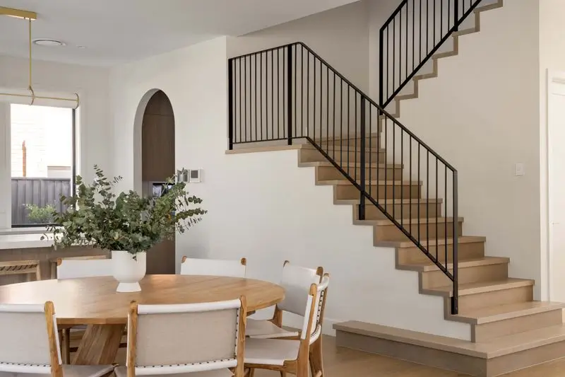 A wooden dining room table with chairs and a staircase in the background