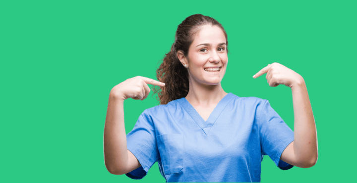 Smiling healthcare worker in scrubs pointing at herself on a green background