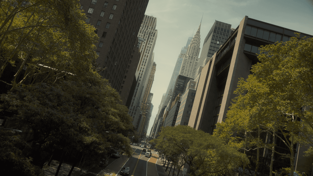 A view of two tall buildings rising above a green park, with trees in the foreground and a clear sky above