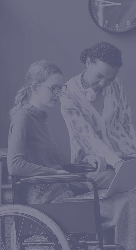 A young woman in a wheelchair and another woman sitting on a sofa while collaborating together on their laptops