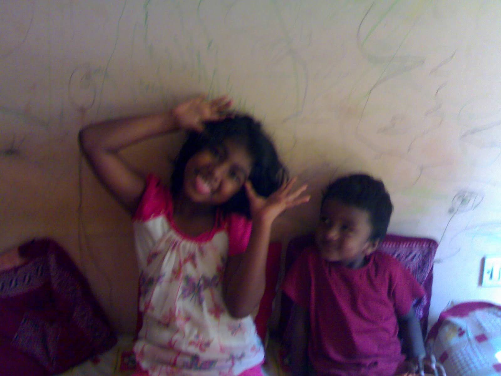 Two children making funny faces, one with tongue sticking out, standing in front of a light-colored wall.
