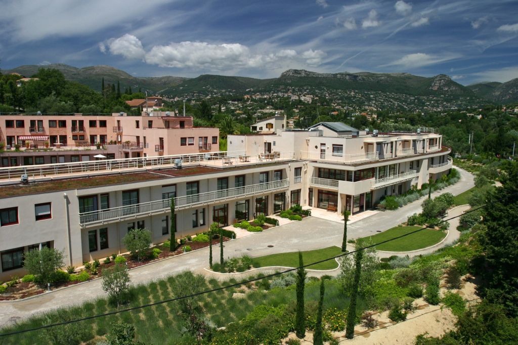Modern rehabilitation facility with Mediterranean-style architecture, green landscaping, mountain backdrop, and bright natural light