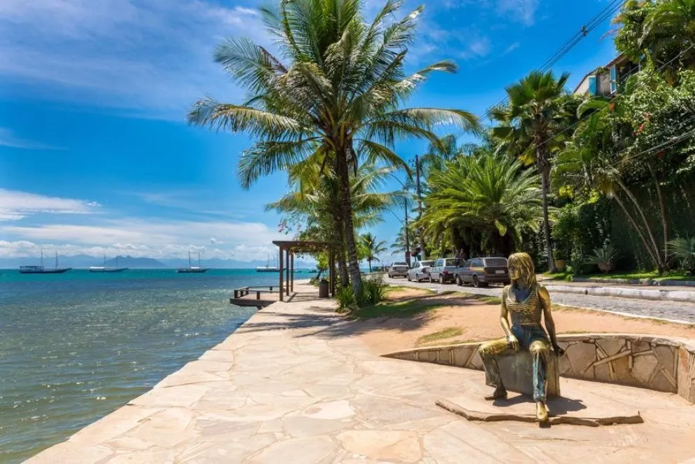 A sophisticated lounge terrace with curved white stucco walls, stone seating, and arched cutouts perfectly framing an unobstructed ocean sunset.