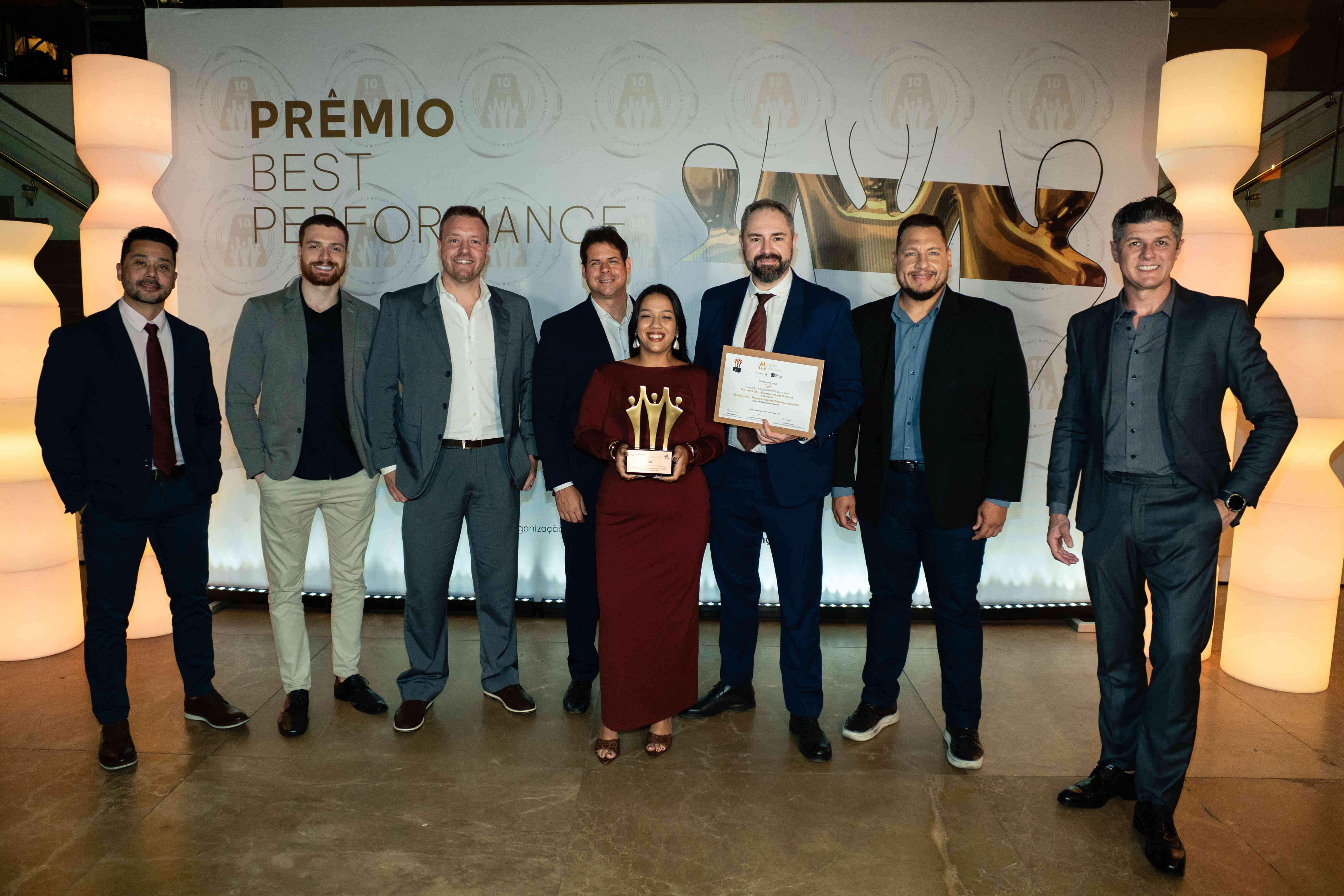 Executivos da Tel posando com troféu bronze e certificado no palco do Prêmio Best Performance 2025.