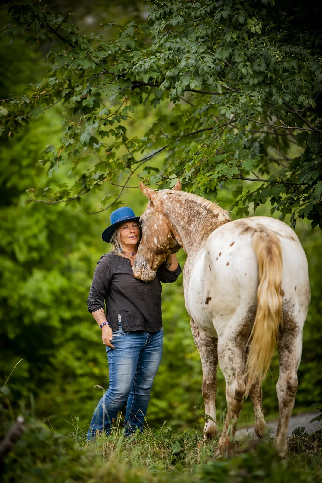 Daya con il cappello blu accanto a un cavallo dal mantello maculato