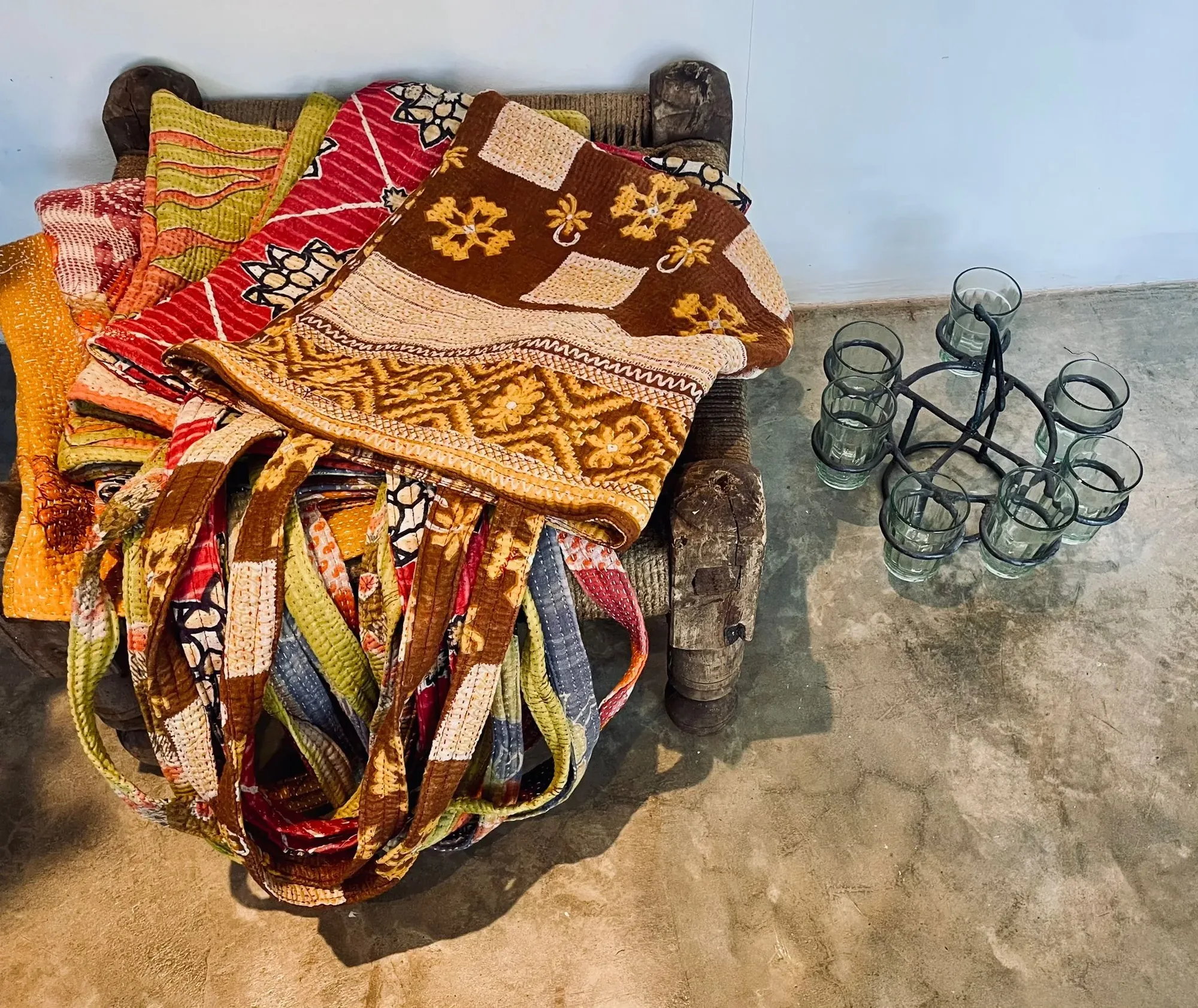 Stack of folded vintage kantha quilts on a rope charpai beside a wrought-iron tealight holder at Jaali Boutique