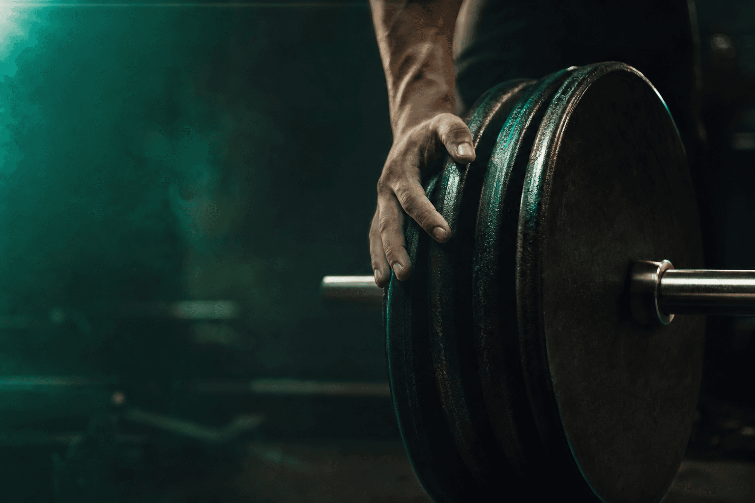 Close-up of a lifter's hand sliding weight plates onto a loaded barbell in a dark gym