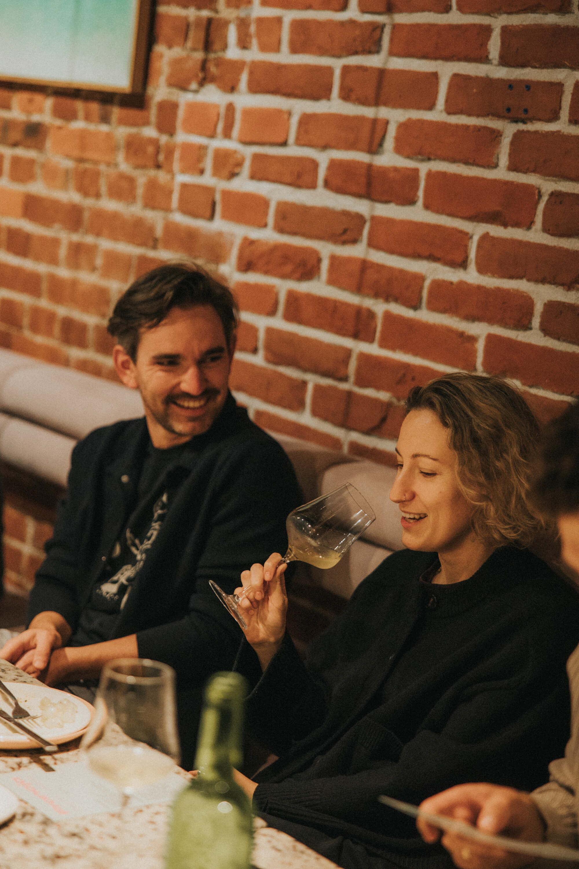 Two people enjoy a conversation over dinner at a cozy restaurant with a brick wall backdrop.