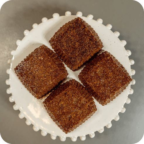 Brownies cuadrados sobre un plato blanco con borde decorado, mostrando su textura húmeda y corteza crujiente.