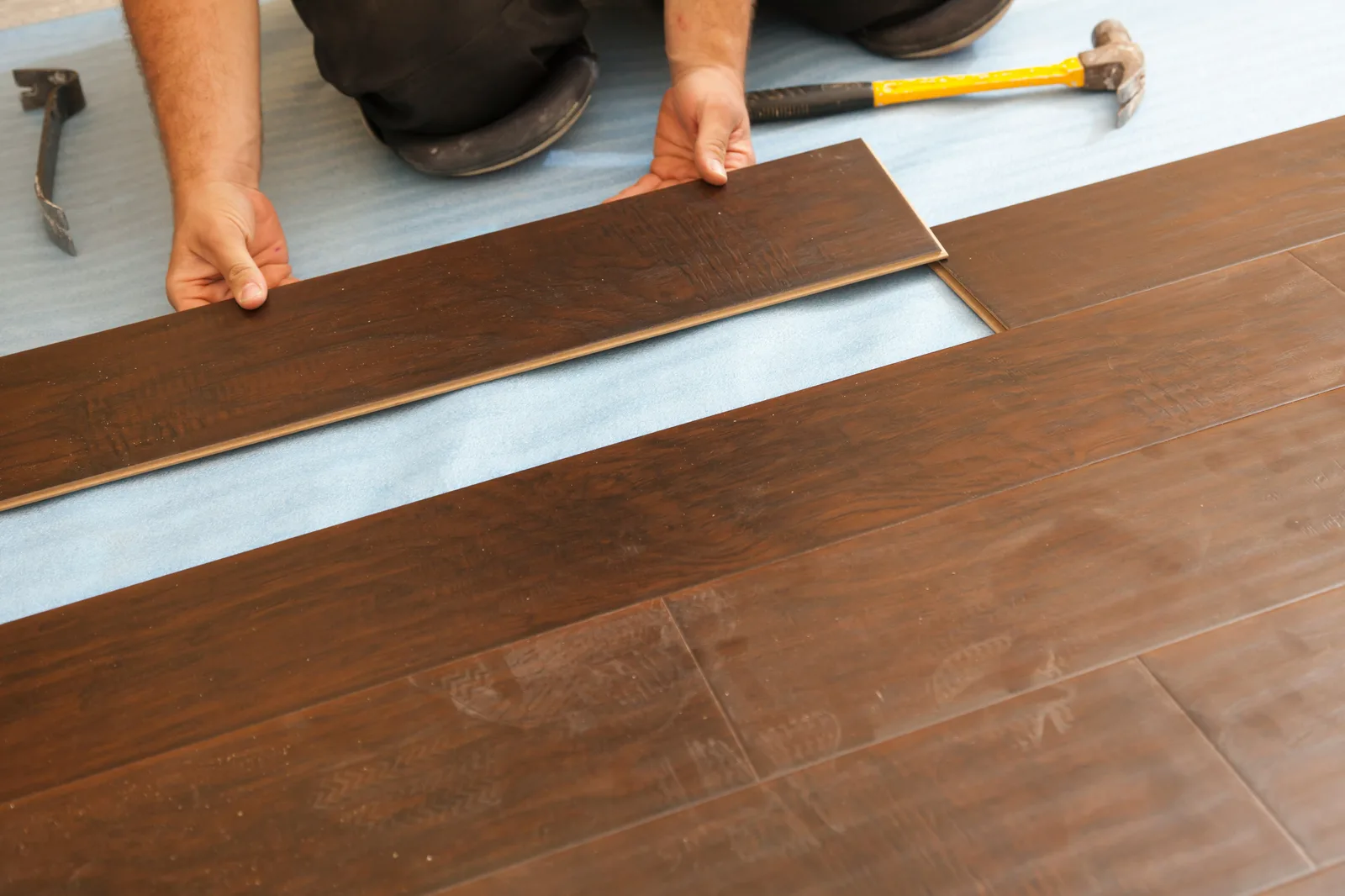 Worker fitting dark hardwood laminate plank with hammer on floor