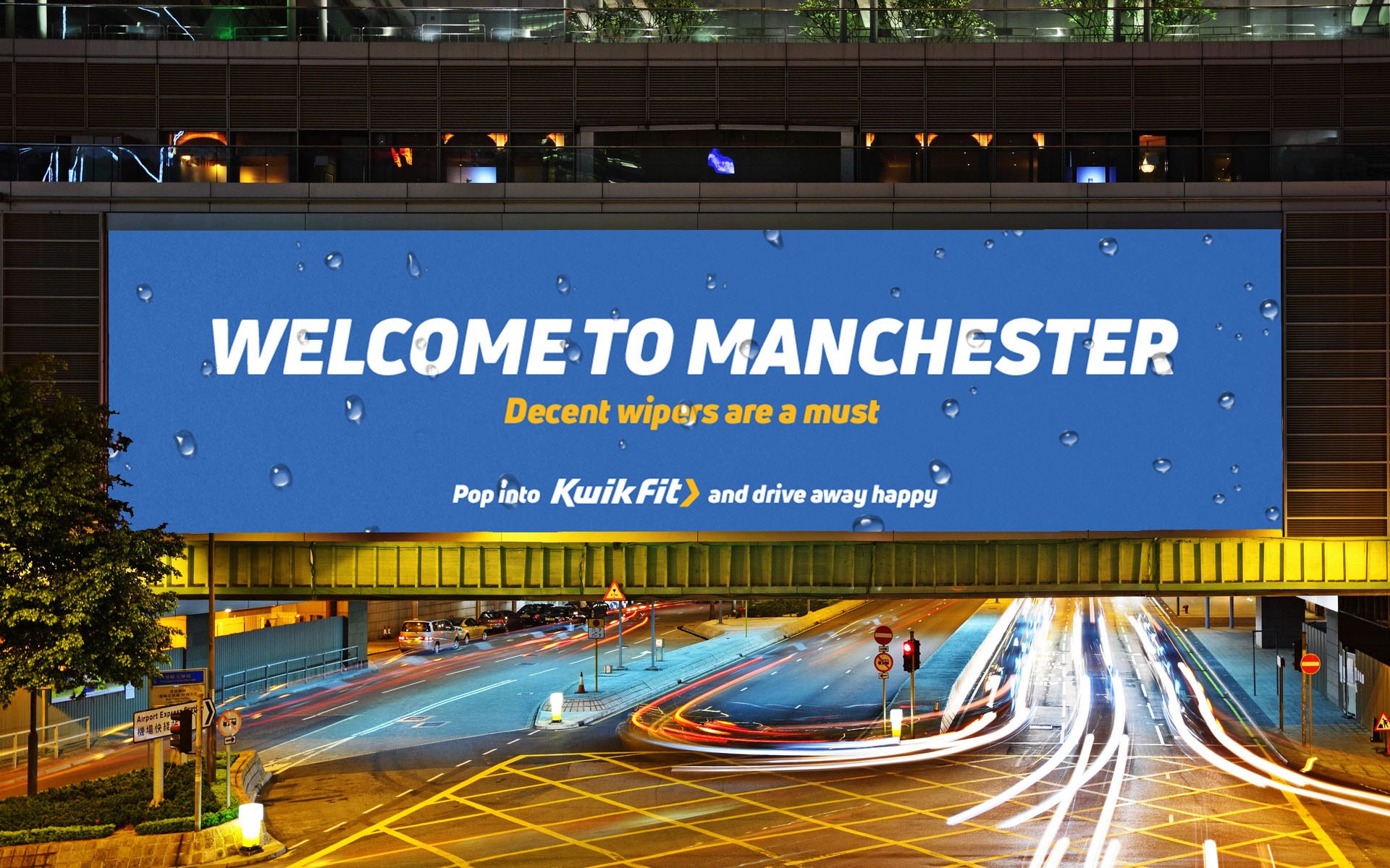 Large 96 sheet billboard above a road that has rain drops on it and reads Welcome to Manchester decent wipers are a must