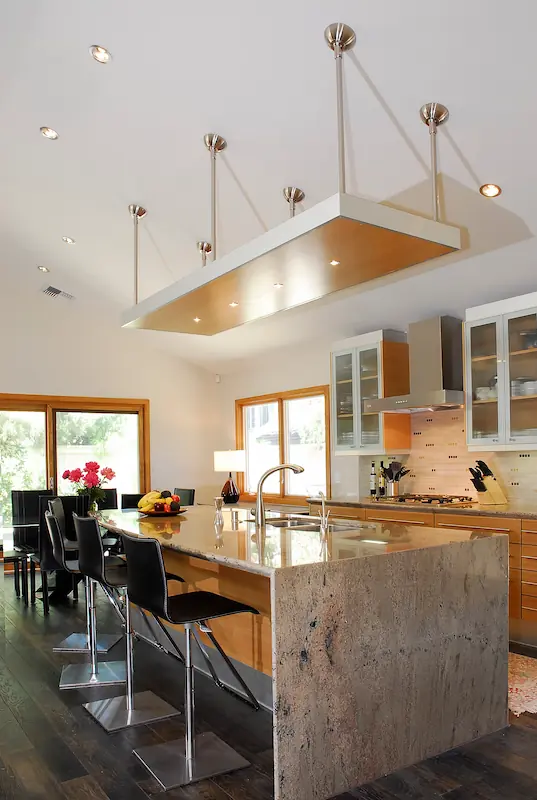 Modern kitchen island with waterfall edge quartzite countertop and clould lighting enclosure with modern yellow wood finish.Modern kitchen with wooden cabinets, central island, hanging lights, and dark flooring. Irvine Transitional Modern. Photo by Chris Darnall.
