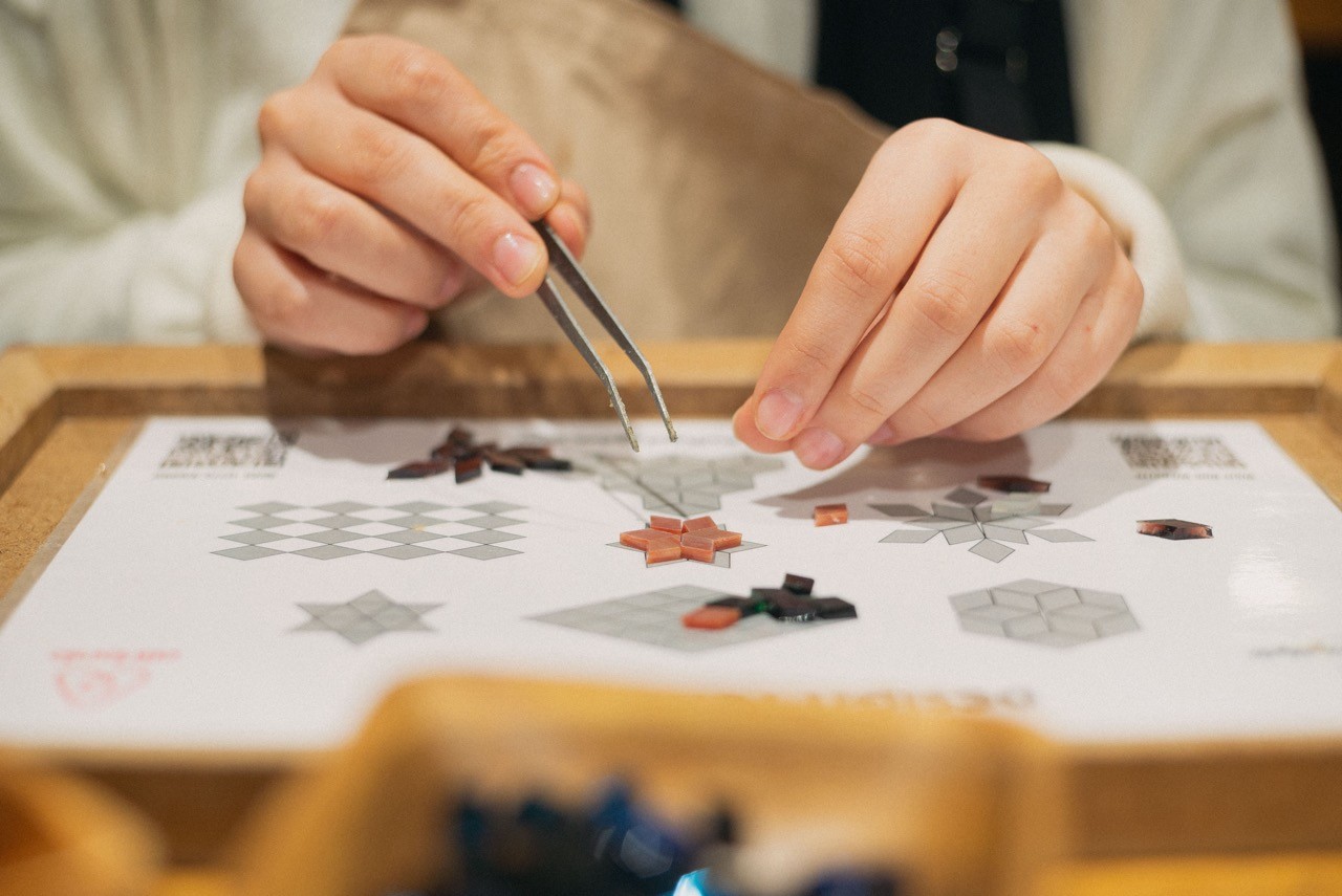 Close-up of hands carefully placing small mosaic pieces onto a template during a Turkish Mosaic Lamp Workshop in Istanbul.