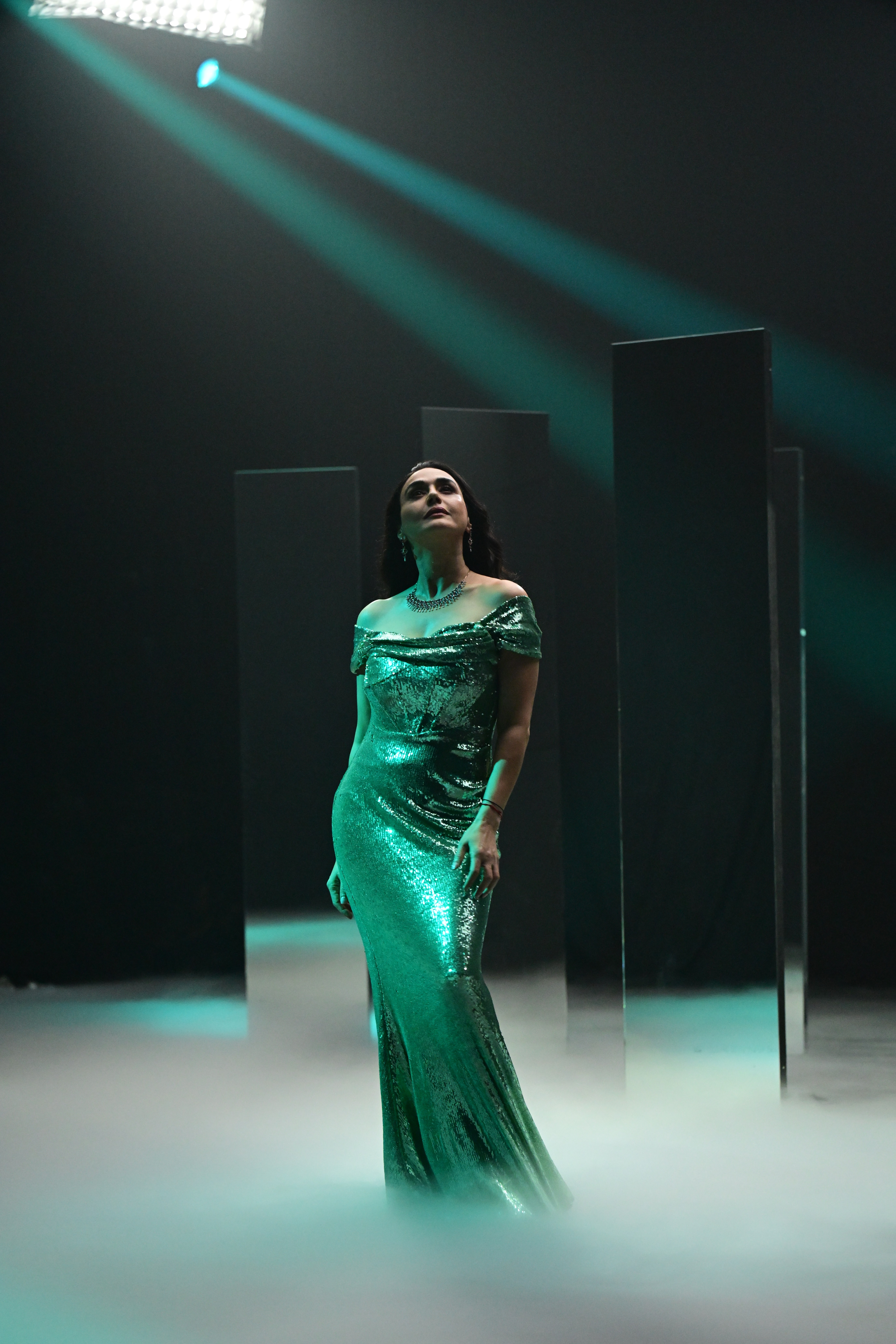 Close-up portrait of a person wearing a gray insulated hooded jacket with the hood up, showing their face framed by the hood against a light background.