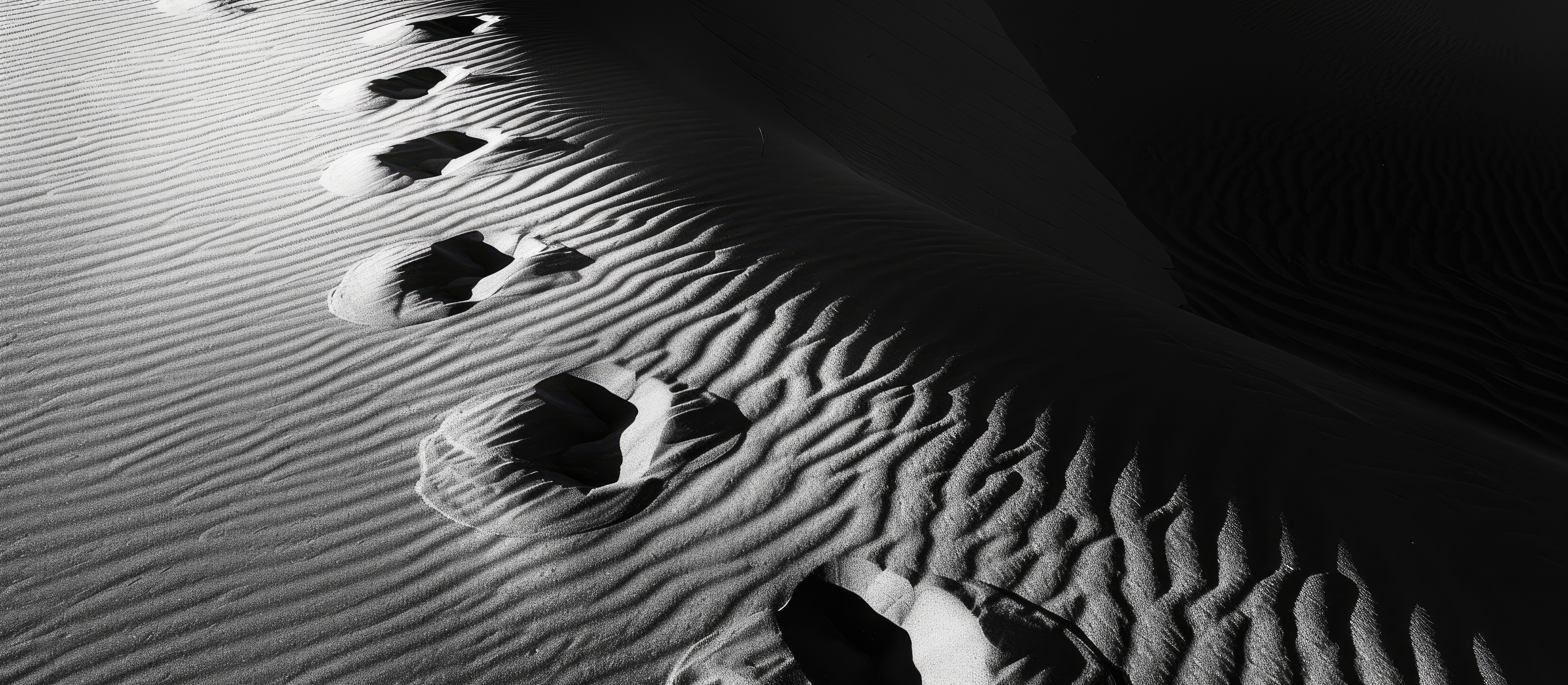 Black and white shot of sand dunes with footprints and shadows.