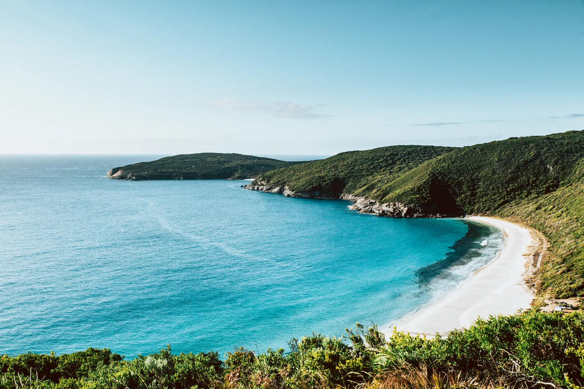 A sheltered turquoise bay enclosed by green headlands, seen from a clifftop