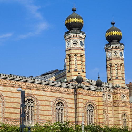 Un grande edificio in mattoni con due alte torri, ciascuna sormontata da una cupola nera e dorata, stagliato contro un cielo azzurro limpido.