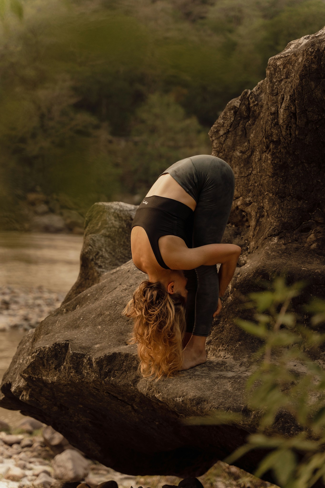 Woman practicing outdoor yoga on a rock in a scenic nature setting.