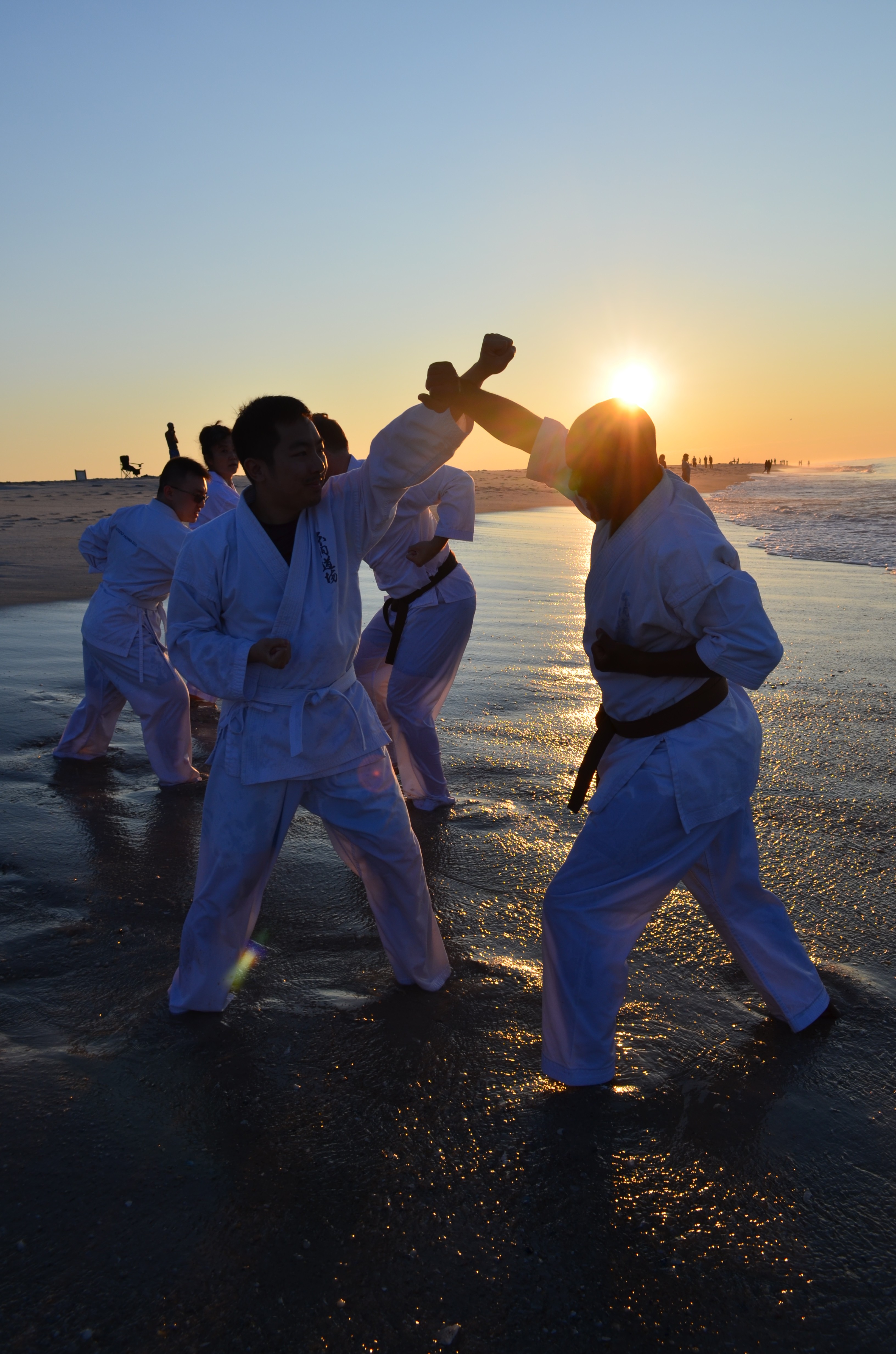 Wooden outdoor table set with multiple plates of food, including dips, salads, potatoes with cheese, and glasses of water, with hands reaching in to eat.