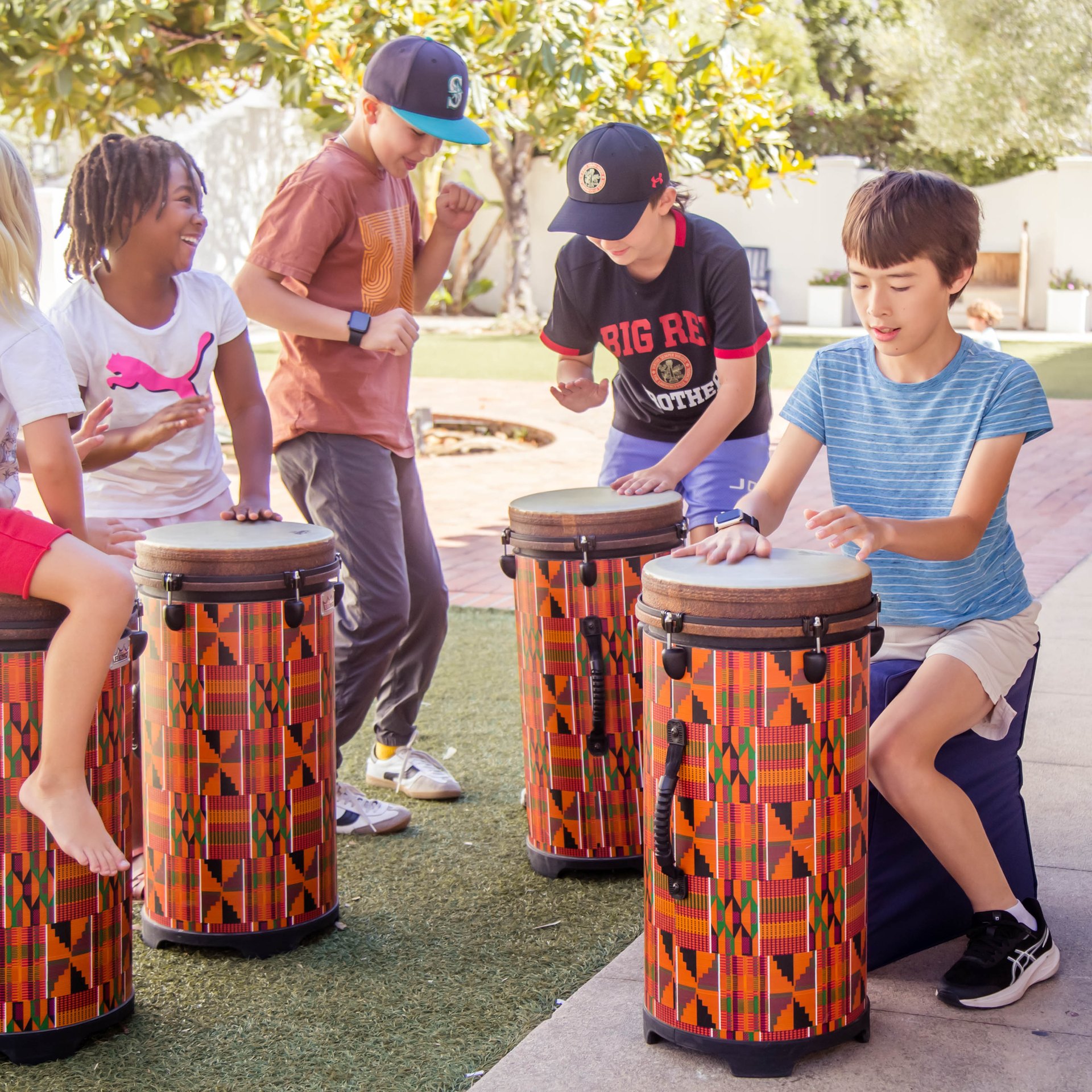 Group of students drumming together on patterned drums in the school courtyard