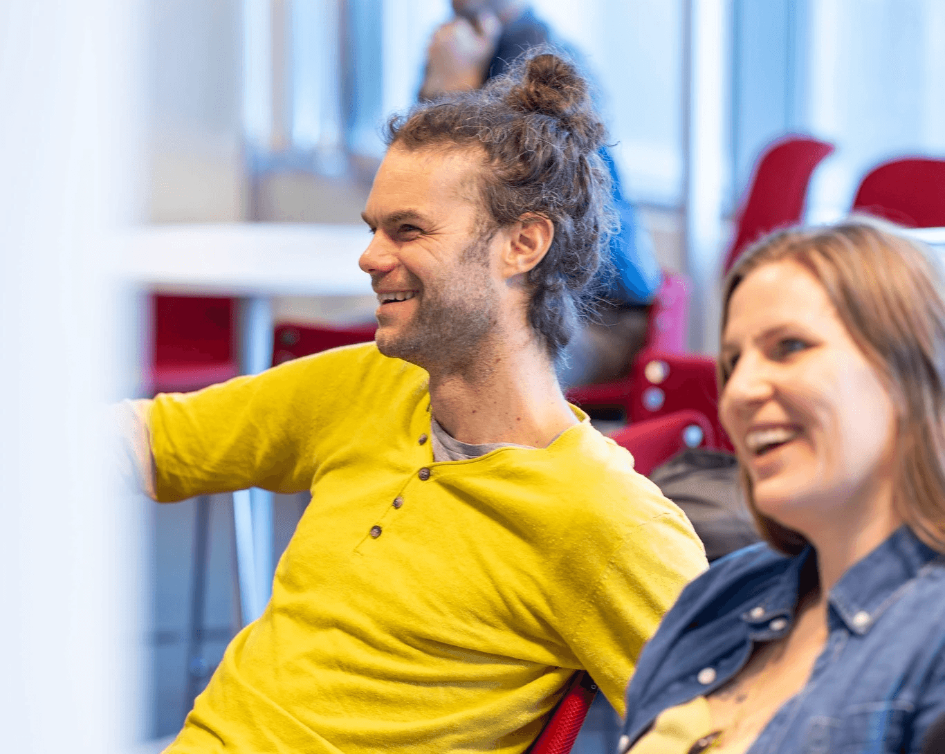 A group of people cheerfully posing together in a brightly lit room, with a red carpet and playful expressions.