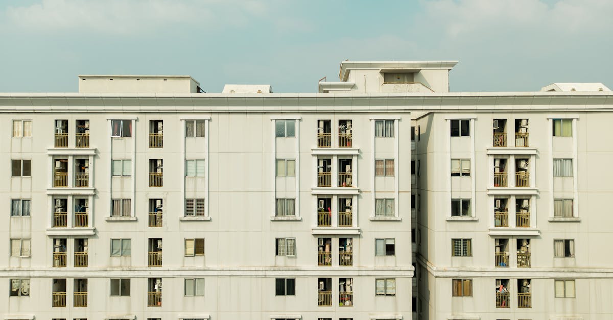 Facade of a white multi-storey apartment block with uniform windows and balconies against a blue sky