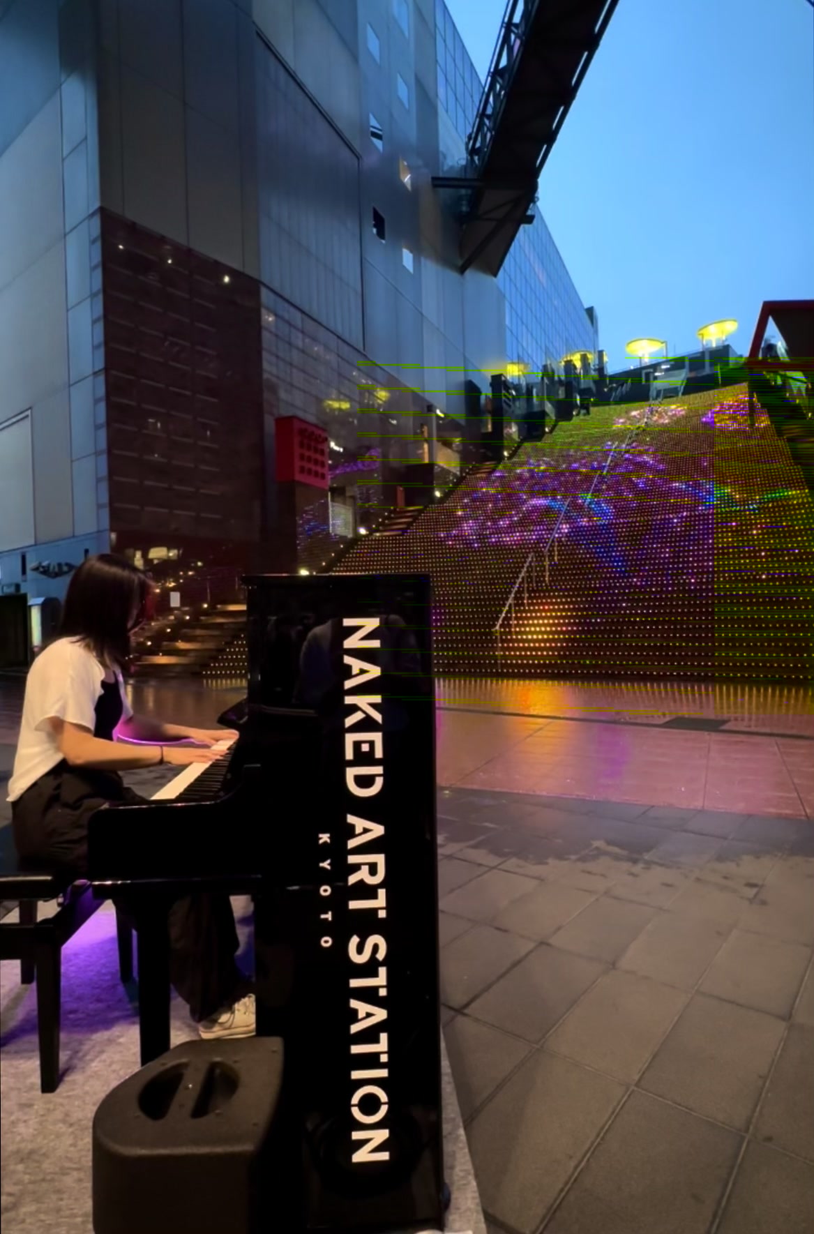 Jess Fong playing piano in kyoto train stations, colorful lighted staircase in the back