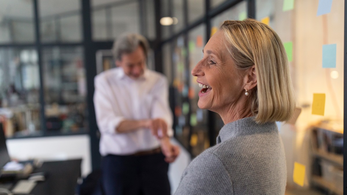 Meeting facilitator standing a front of a glass wall filled with sticky notes and smiling