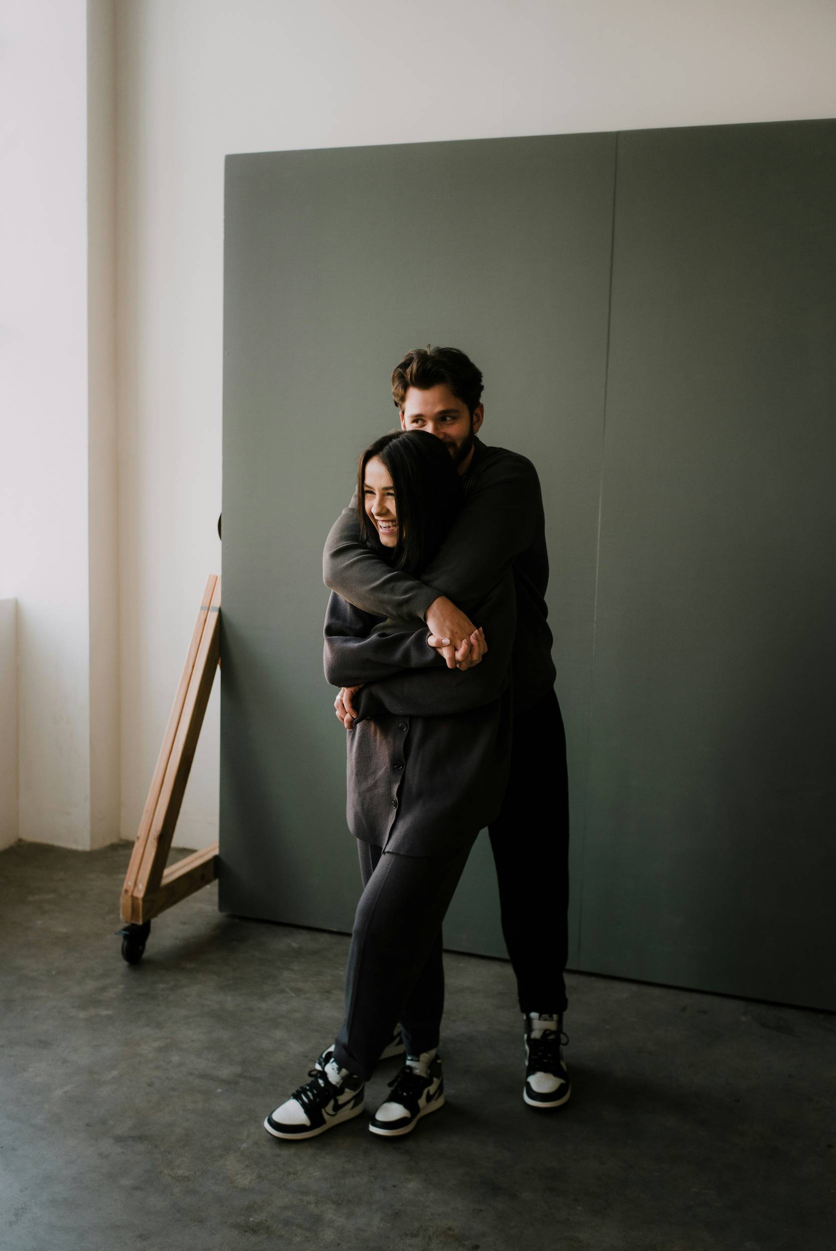 A man hugs a woman from behind in a studio while they laugh