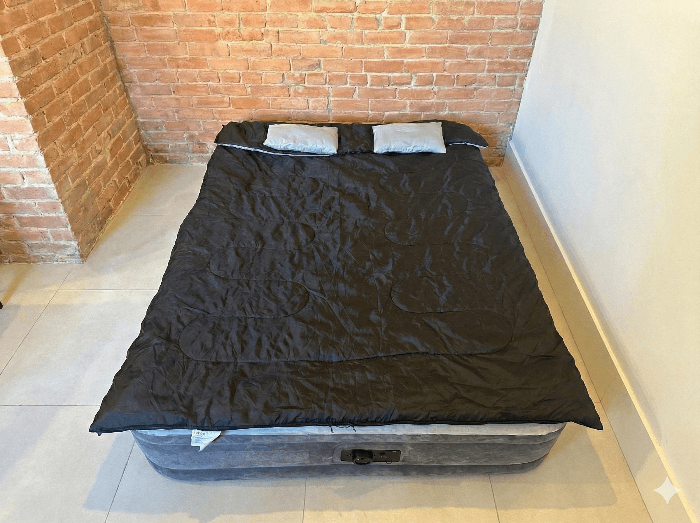 Duvet double noir posé sur un matelas gonflable Intex pour deux personnes, avec deux oreillers, installé dans une pièce en briques à Montréal.