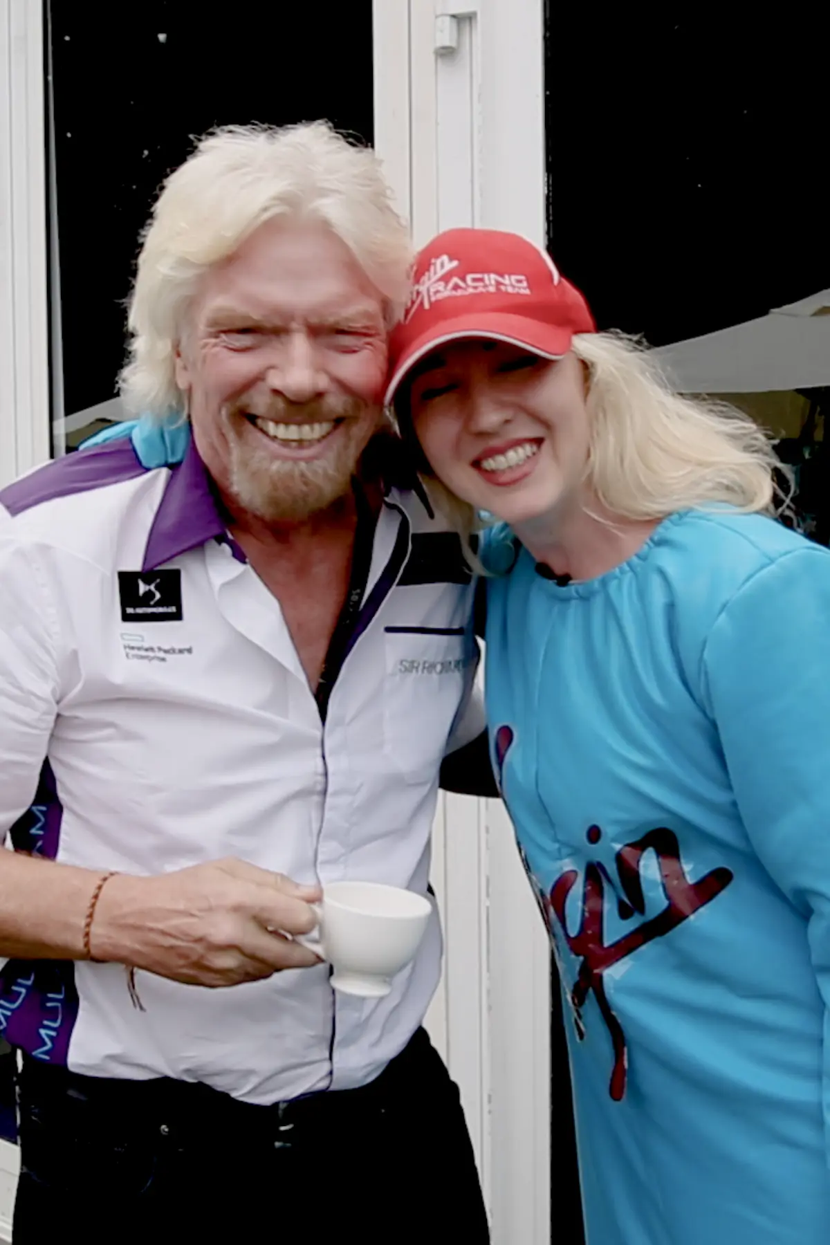 Richard Branson holding a coffee cup while speaking with Agent Blonde wearing an alien costume during the documentary