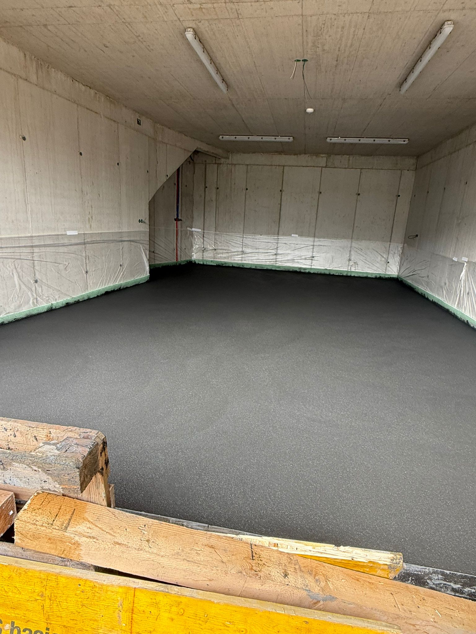 Fertigbetonboden einer großen Tiefgarage mit Leuchtstoffröhren.
