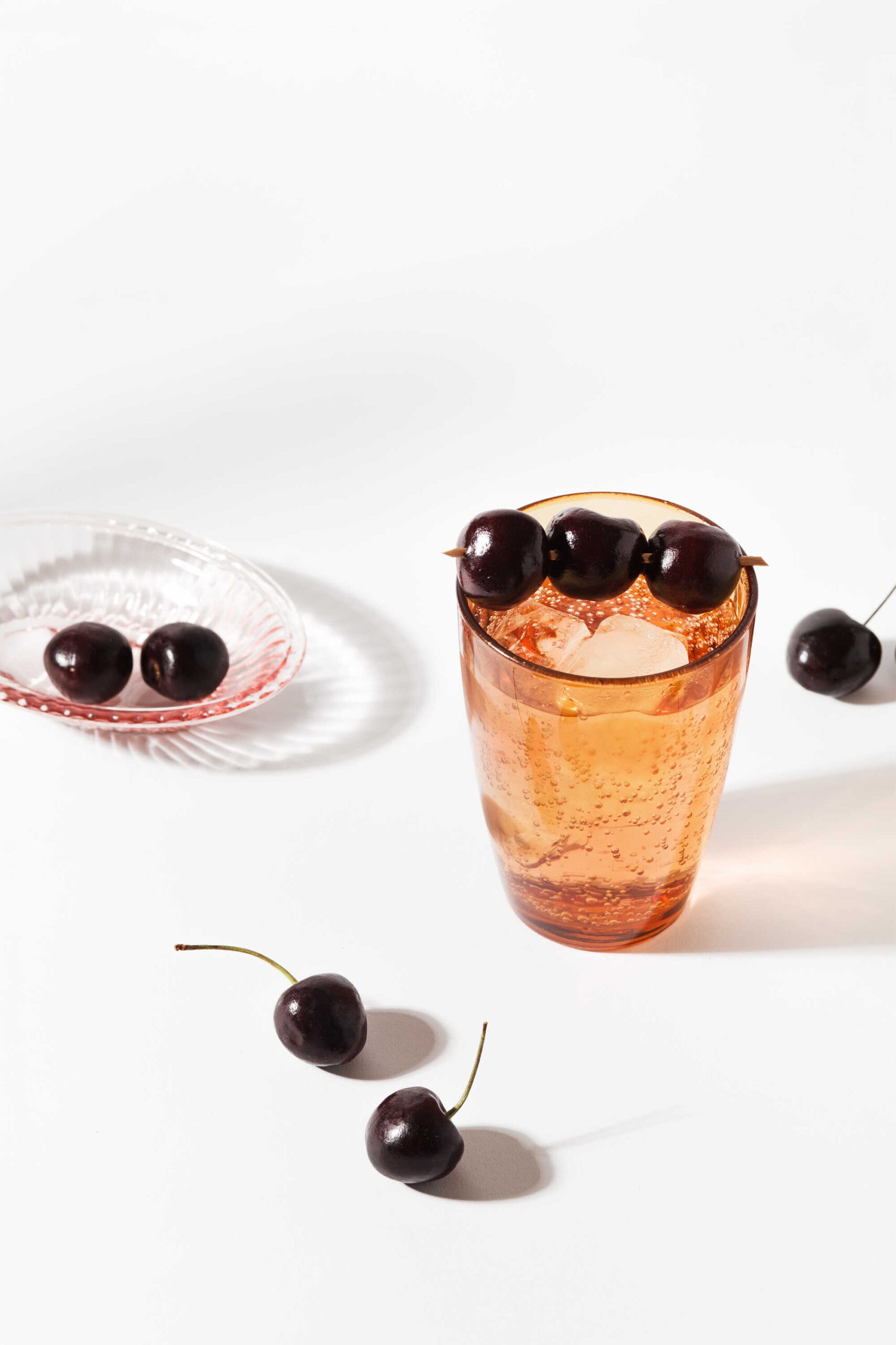 A tall cocktail glass filled with vodka, tonic, ice cubes, and garnished with cherries—served as the Cherry on Top cocktail.