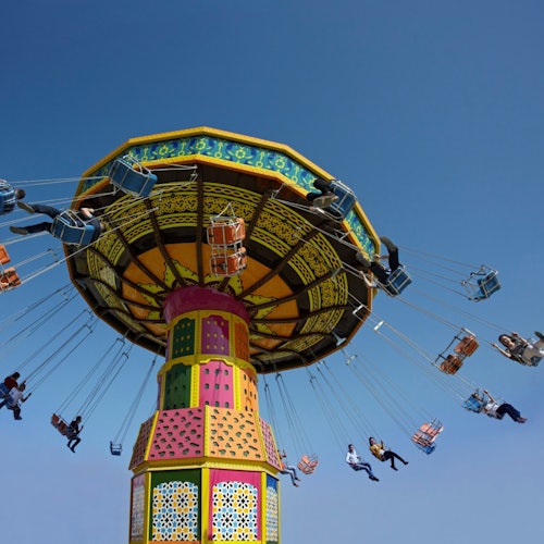 Mga tao na sumasakay sa makulay na swing carousel sa ilalim ng maliwanag na asul na langit.