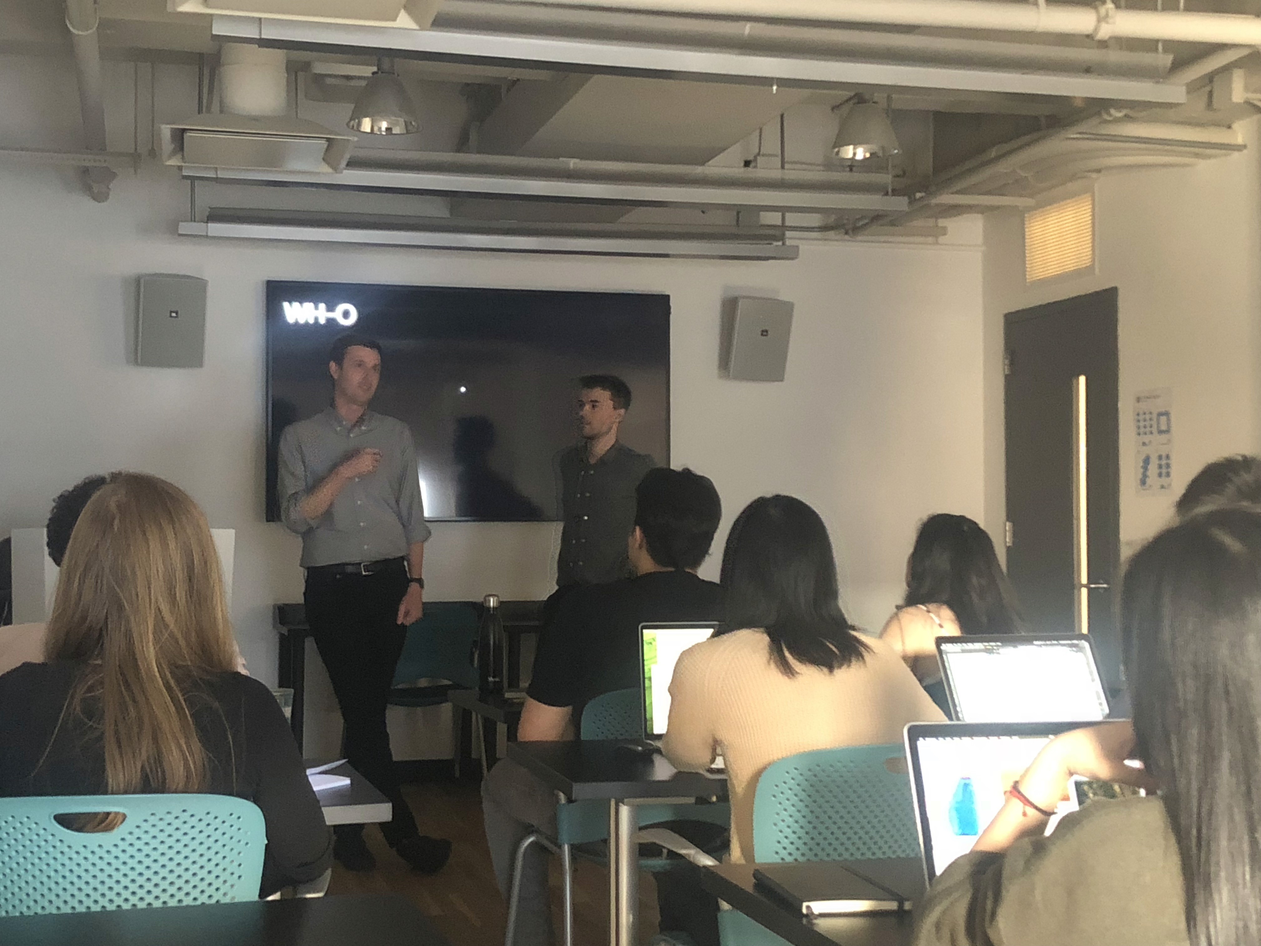 A photo of some students in a classroom listening to a lecture, held by two people.